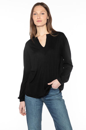 A woman with straight brown hair is wearing a black, long-sleeved KINROSS CASHMERE - SPLIT NECK SILK AND CASHMERE PULLOVER along with blue jeans. She is standing against a white background with her left hand in her jeans pocket and her right arm relaxed by her side. She has a neutral facial expression.