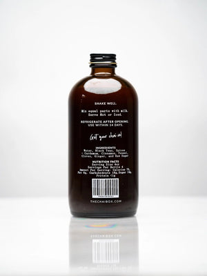 The Chai Box's brown glass bottle, prominently labeled with "THE CHAI BOX - CHAI CONCENTRATE," features text that reads "Hand crafted in small batches" and specifies a volume of 16 fl oz / 473 ml. Made with the finest spices, the label proudly displays "Atlanta, GA" at the bottom. The bottle is topped with a black screw cap.