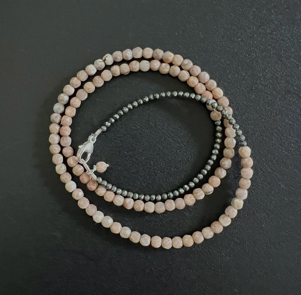 The ANN LIGHTFOOT bracelet features sunstone and pyrite beads arranged in a circular pattern on a dark surface, with an elegant design enhanced by a small sterling silver clasp.