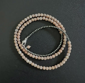 The ANN LIGHTFOOT bracelet features sunstone and pyrite beads arranged in a circular pattern on a dark surface, with an elegant design enhanced by a small sterling silver clasp.