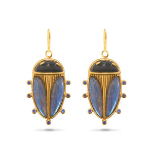 The CAPUCINE DE WULF Scarab Petite Drop Blue Labradorite/Black Agate Earrings by Capucine de Wulf feature a pair of gold drop earrings designed to resemble beetles. Adorned with black agate and iridescent blue labradorite stones, they include six small circular blue accents along the edges and each earring is attached with an 18K gold hook.