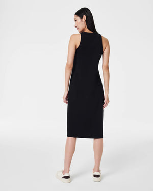 A person with long dark hair is standing against a plain white background, facing away from the camera. They are wearing the SPANX - AIRESSENTIALS SIDE STRIPE MIDI DRESS, a sleeveless black knee-length piece crafted from light-as-air fabric. The dress is stylishly paired with white sneakers, offering an elegant blend of comfort and style.