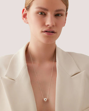 The JENNY BIRD - AURORA PENDANT NECKLACE by JENNYBIRD features a minimalist design with a sleek silver chain and a single high-polish silver bead at its center, elegantly suspended by a subtle slider closure against a plain white background.