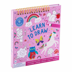 An open *FLOSS AND ROCK - RAINBOW FAIRY LEARN TO DRAW* kit by *FLOSS & ROCK*, featuring an eco-friendly "Learn to Draw" book with step-by-step instructions for drawing a mushroom on the left page. On the left side are three markers in yellow, blue, and white. The right side of the kit showcases a finished drawing of a pink and yellow mushroom with polka dots.