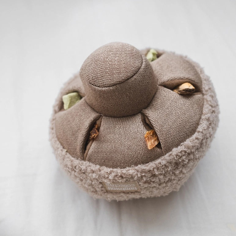 A small, plush button mushroom toy from LAMBWOLF COLLECTIVE. The cap is covered in a fuzzy, textured fabric, while the stem and gills are made from a smoother material in a matching beige color. Designed by LAMBWOLF COLLECTIVE to look cute and cuddly, this washable pet toy is perfect for both playtime and snuggles.