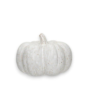 A trio of white speckled stoneware pumpkins from the Creative Coop brand, featuring various sizes, is beautifully arranged on wooden logs of differing heights. This delightful home decor piece rests on a beige surface adorned with scattered wood shavings and is set against a textured, light-colored background.