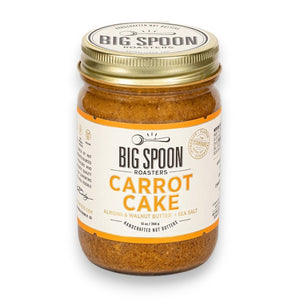 A 13-ounce (369 grams) jar of BIG SPOON ROASTERS - CARROT CAKE nut butter with sea salt. The jar features a white label adorned with orange accents and the BIG SPOON ROASTERS logo at the top. This vegan, handcrafted spread, rich in heart-healthy fats, is sealed with a gold lid.