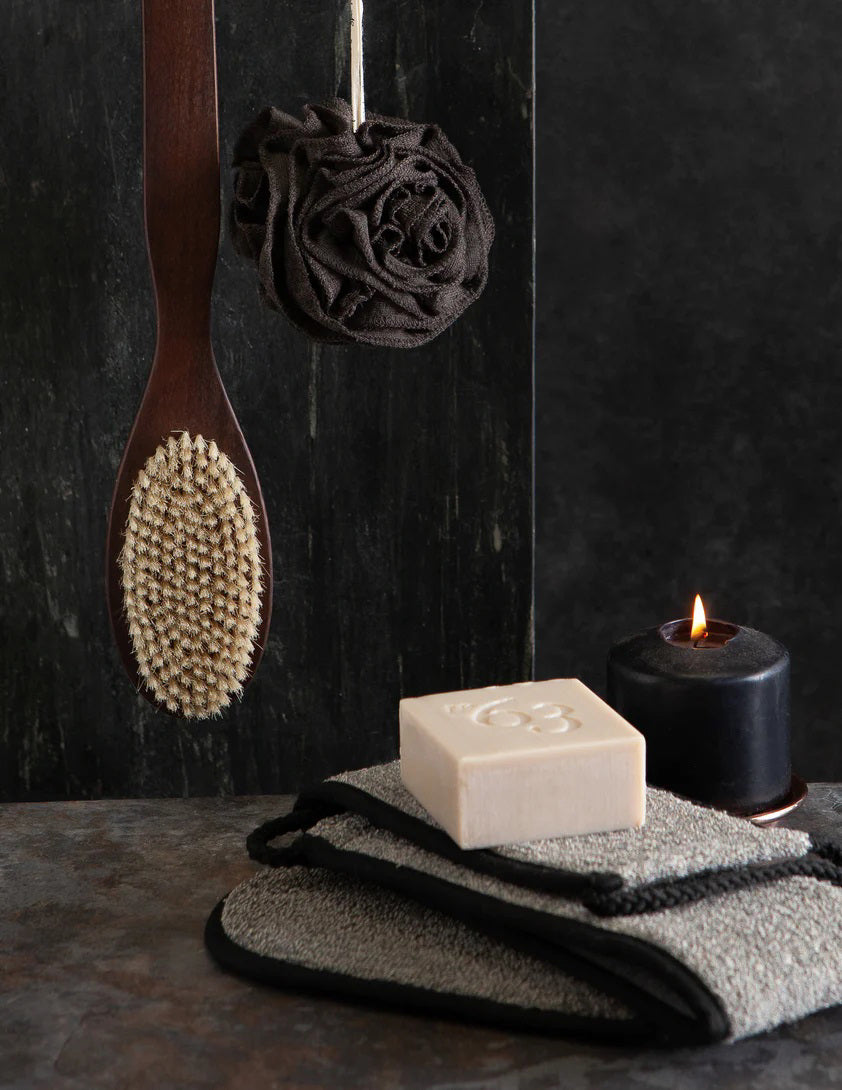 A black bamboo pouf, an eco-friendly bath accessory, nestled inside grey and gold packaging. The label reads &quot;EUROPEAN SOAPS, LLC&quot; with a sleek design that includes geometric patterns and the words &quot;Hommes&quot; and &quot;Spa Privé&quot;.