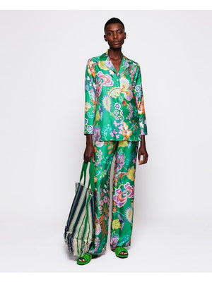 A person in MIRTO 1956's silk floral pant, featuring an elastic waistband, holds a large striped tote bag. Complementing the outfit are matching green sandals, all set against a plain white background.