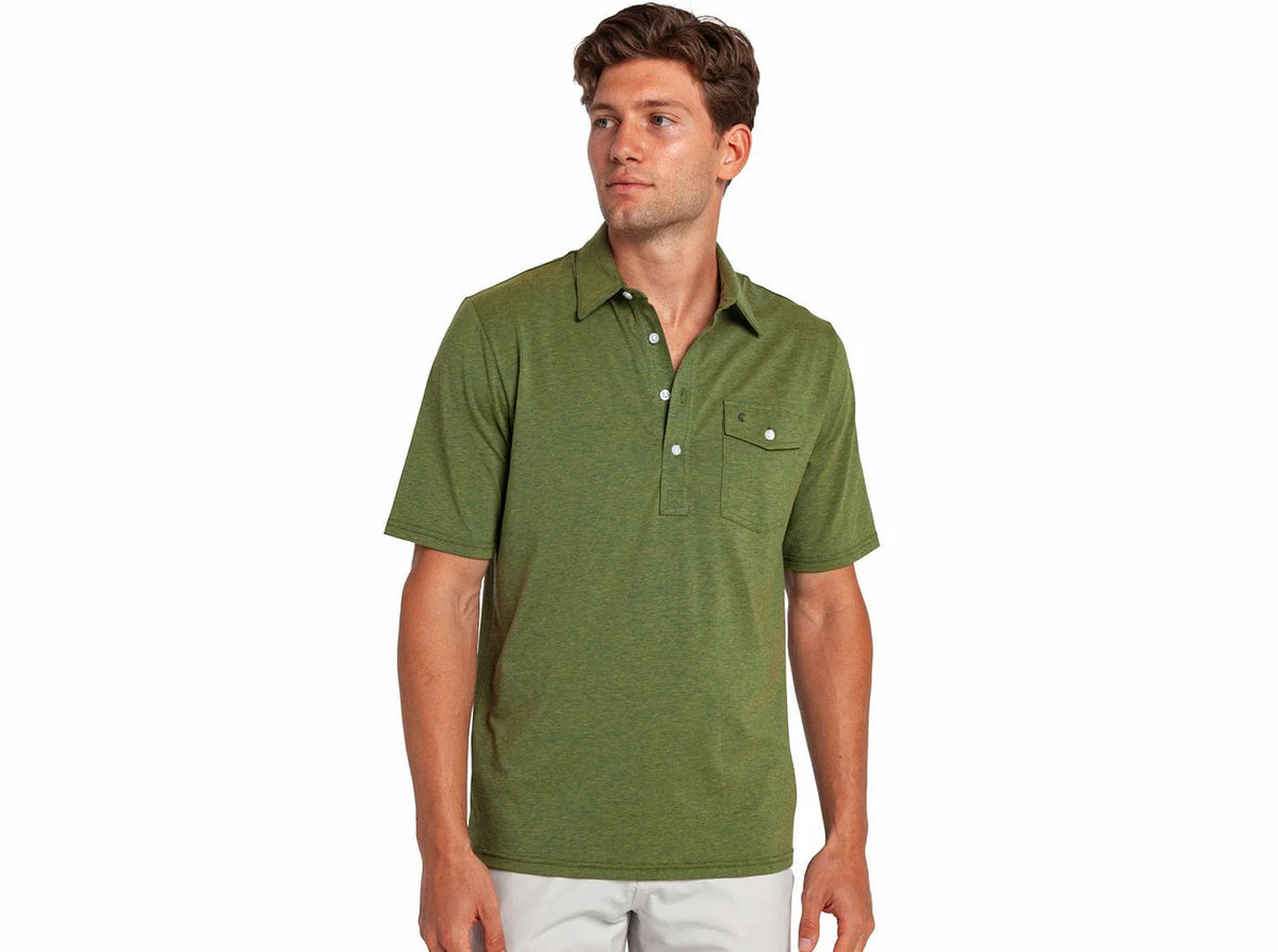 A young man wears a CRIQUET Performance Players Shirt in Groundskeeper—a classic-fit, short-sleeved green shirt with buttons and chest pocket—as he stands looking slightly left against a plain white background.
