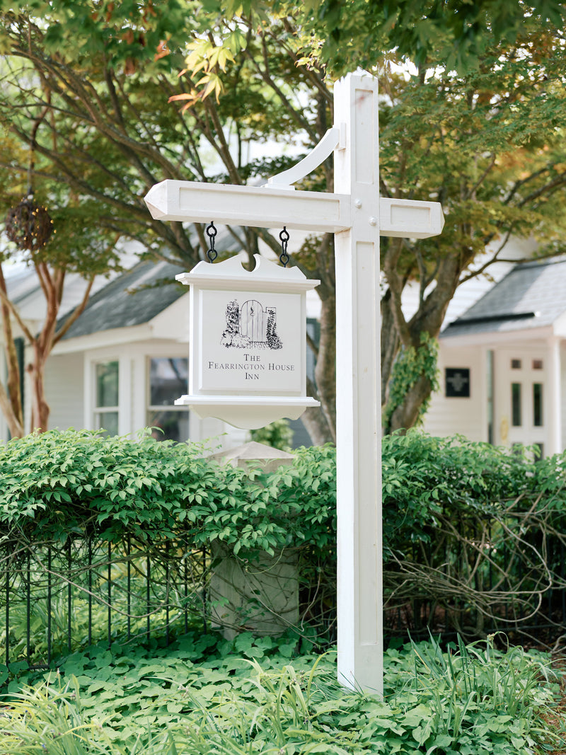 A white wooden signpost displays a hanging sign for 
