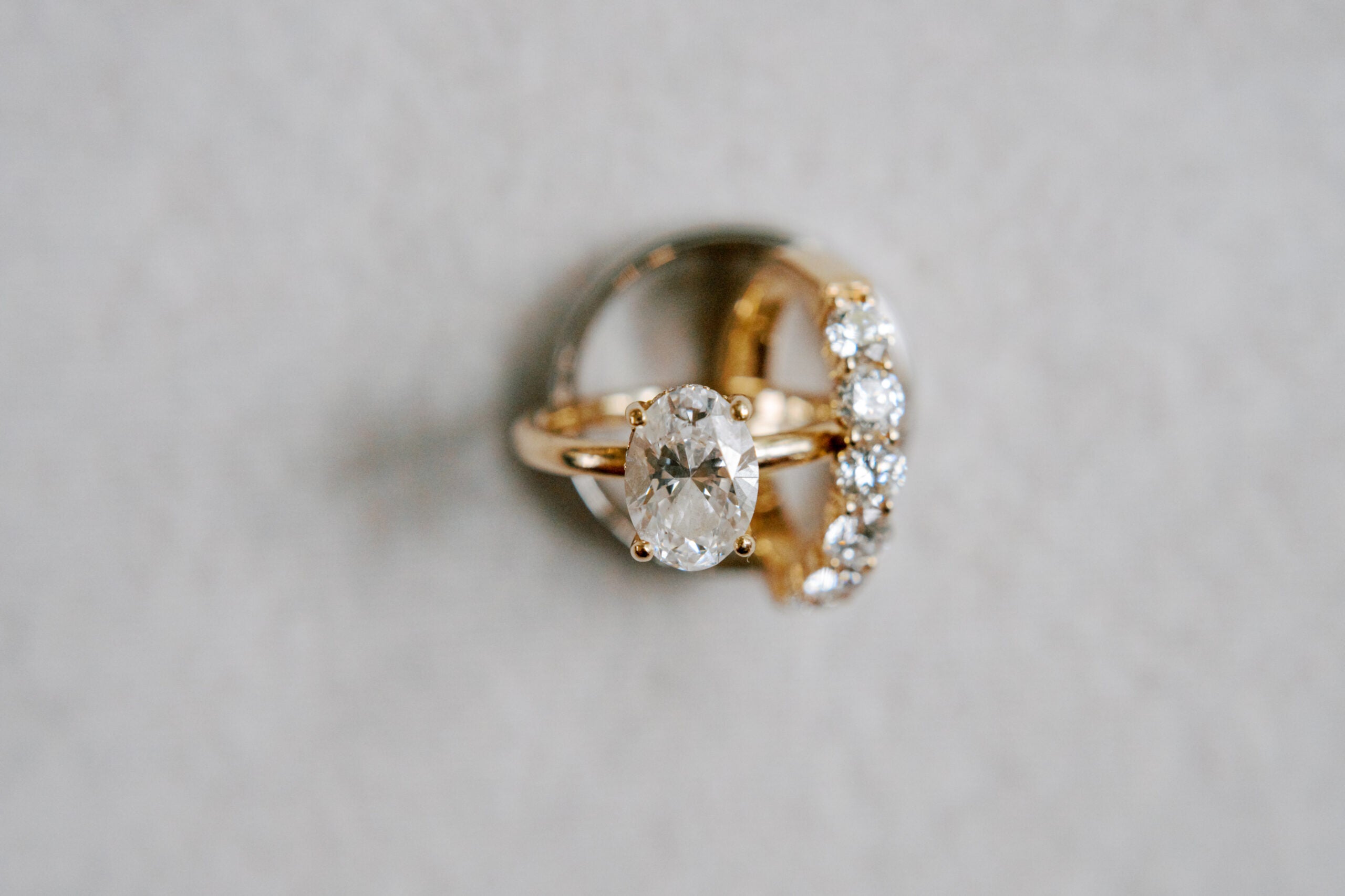 Two gold rings on a light, textured background: one features a large oval diamond solitaire, and the other is set with five round diamonds in a row.