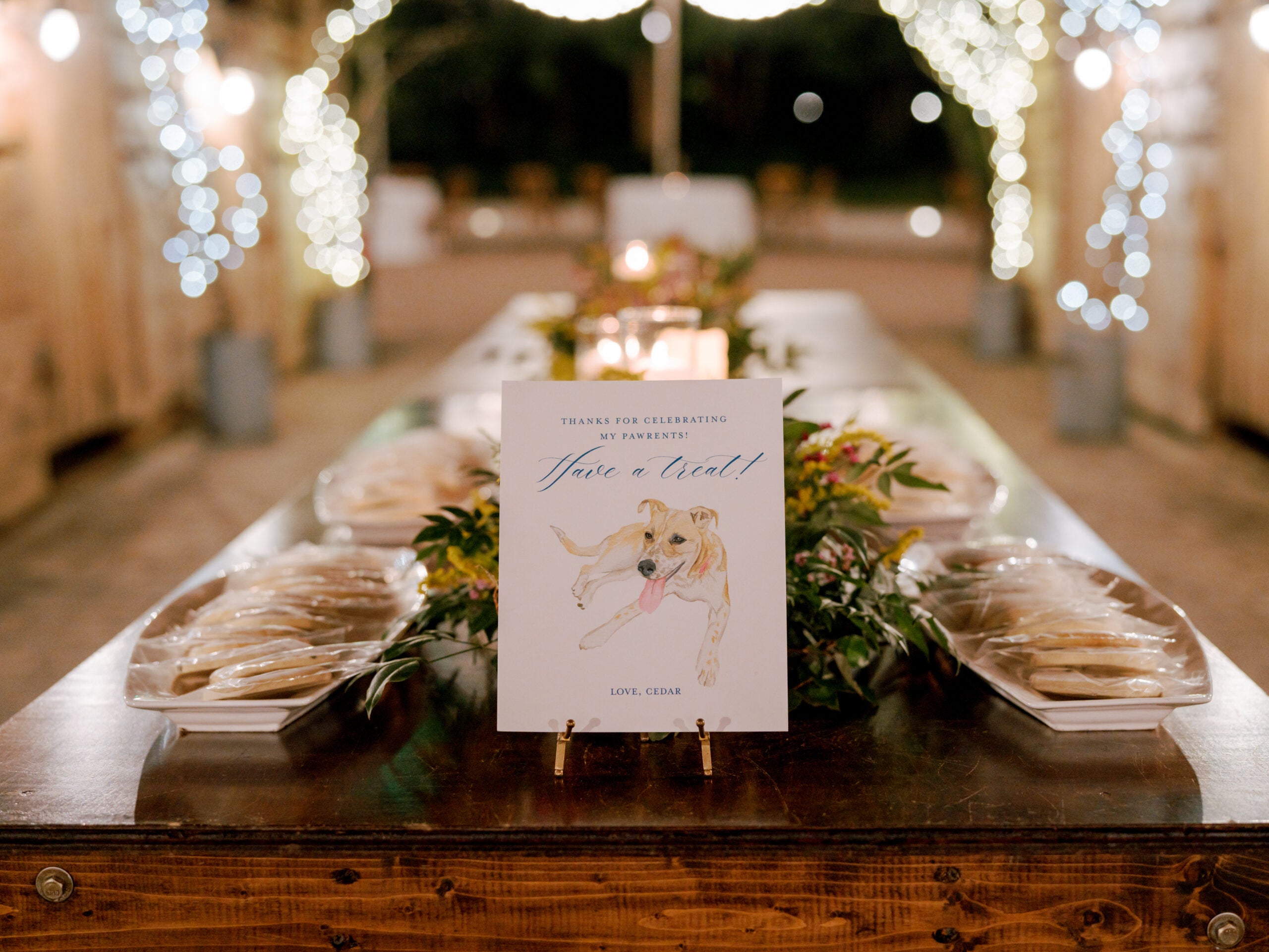 A decorated table set outdoors at night features a sign with a dog illustration reading 