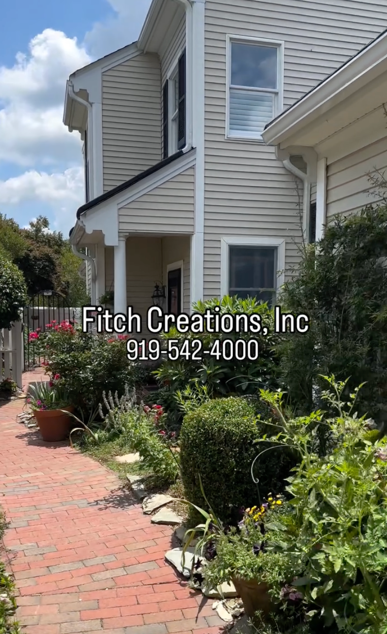 A beige house with white trim and a garden of flowers and shrubs along a brick pathway. Text overlay reads: 