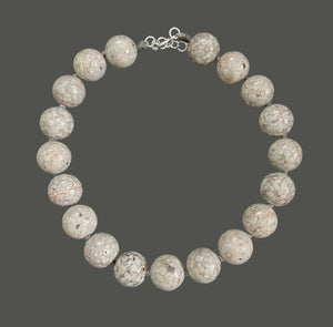 The ANN LIGHTFOOT Fossil Coral Ras du Cou Necklace features large, polished round fossil coral beads in light gray and beige with circular patterns and a sterling silver clasp, shown on a dark gray background.