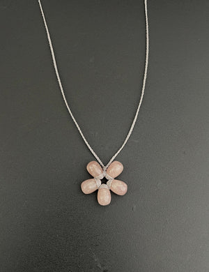 The ANN LIGHTFOOT - PETITE SUNSTONE FLOWER NECKLACE features a flower-shaped pendant with six pinkish-brown oval stones on a thin twisted metal chain. This adjustable necklace adds elegance to any outfit and is set against a plain white background.