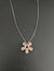 The ANN LIGHTFOOT Petite Sunstone Flower Necklace features a flower-shaped pendant with five pink stone petals and a central white stone on a dark setting. It has a delicate silver chain and adjustable nylon ties for the perfect fit.