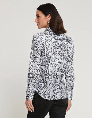 A person with long dark hair, wearing a fitted HINSON WU Diane Long Sleeve Snow Leopard Print Sateen Shirt in white and black, along with black pants, standing and facing the camera with a neutral expression. The background is plain light gray.