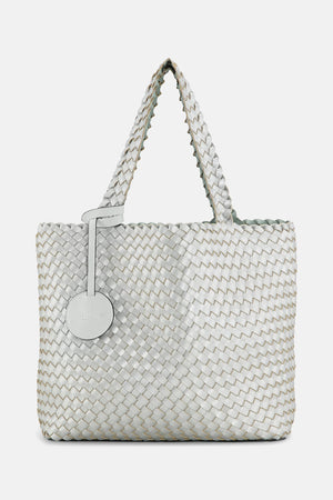 The WOVEN REVERSIBLE TOTE BAG by LINES OF DENMARK is a white tote featuring two shoulder straps and a circular faux-leather tag on one strap. This shopper showcases a textured, interlaced pattern and reversible design, providing stylish and elegant dual styling options. The image background is plain white.