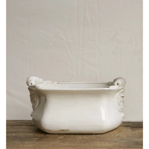 Introducing the LARGE TERRACOTTA CACHEPOT IN WHITE by CREATIVE COOP, a rectangular ceramic planter with raised handles on both sides and intricate designs near the corners. This cachepot boasts a slightly weathered, distressed white finish, complete with minor discolorations and worn spots, which add to its rustic charm.