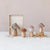 Four FABRIC TOPPED FOAM MUSHROOMS WITH WOOD BASE by CREATIVE COOP are displayed on a white surface. The three smaller mushrooms stand upright, while the largest one leans against the wooden base. The scattered white seeds around them create a whimsical effect, reminiscent of sequins and glitter sparkling in the light.