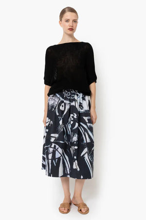 The JUJU CIRCLE SKIRT by TALKING WALLS is an A-line midi-skirt adorned with a striking black and white abstract pattern. It showcases high-end tailoring, featuring a high waist, an elastic waistband, and a pleated design that provides a flowing and voluminous appearance. The bold print includes diverse brush strokes and shapes.