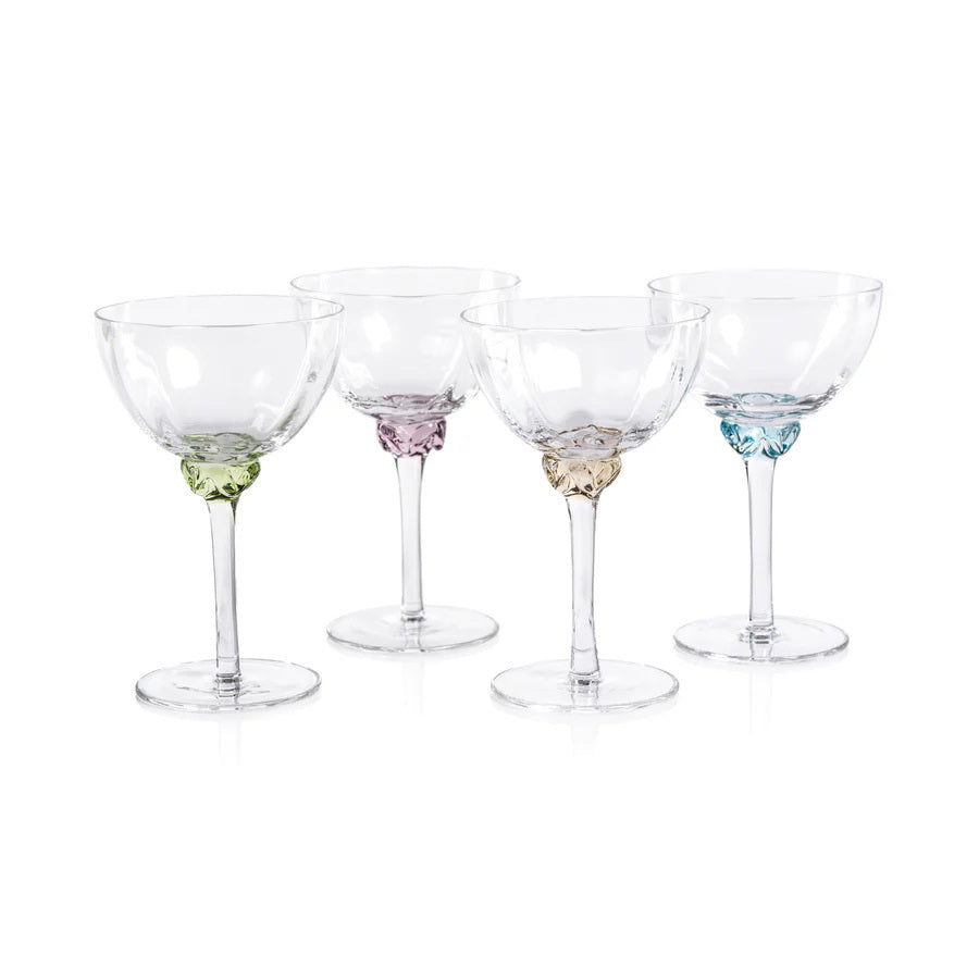 Introducing the MARTINI COCKTAIL OPTIC GLASS by ZODAX: a clear, elegant stemmed glass featuring a shallow, wide bowl. The glass boasts a detailed, decorative stem and a circular base. With a 150 ml capacity, its minimalist and sophisticated design is ideal for serving champagne or cocktails.