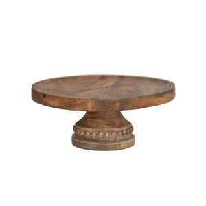 Introducing the Creative Coop "Mango Pedestal with Wood Beads," a wooden cake stand crafted from 100% mango wood. This elegant stand offers a round, flat surface perfect for holding cakes or desserts and features a decorative carved base adorned with circular bead patterns near the top. The natural finish of the mango wood beautifully showcases its unique grain and texture.