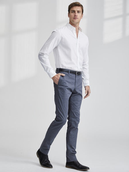A man stands in a minimalist room wearing the FRANK &amp; EILEEN FINBAR Men&#39;s Button Up Shirt in Classic Italian Poplin, tucked into slim-fit blue trousers with a black belt and dress shoes, looking to the side with a neutral expression.