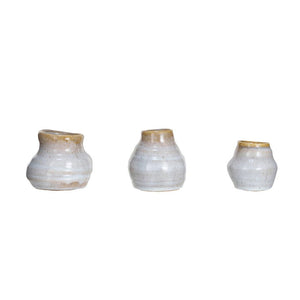 A large, ornate ceramic planter with broad green leaves is accompanied by three small Creative Coop TERRACOTTA GLAZED VASES - LARGE. These reactive-glazed vases are displayed atop stacked white books on a white surface against a light-colored wall.