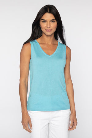 A person with long dark hair in a sleeveless turquoise KINROSS Cashmere Front to Back Silk Cashmere Tank and white pants stands against a plain white backdrop, looking directly at the camera with a neutral expression.