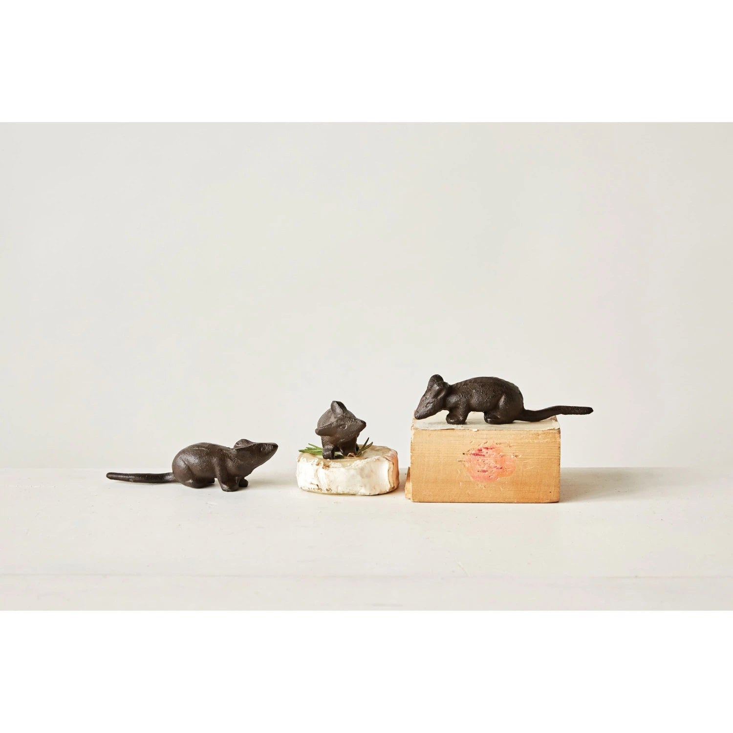 Positioned against a plain white background are three small, dark brown "CAST IRON MOUSE" figurines by CREATIVE COOP. Each measuring 5 inches in length, these figurines feature varied poses and detailed features, conveying a rustic and playful aesthetic through their assorted styles.