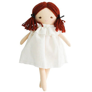 A child wearing a white long-sleeved shirt is seen holding the ALIMROSE - MINI MATILDA ASLEEP AWAKE doll, which has red hair and is snugly tucked into a floral-patterned sleeping bag. The cloth doll features a hood covering its head. The background displays a white textured surface, encouraging developmental play and social skills.