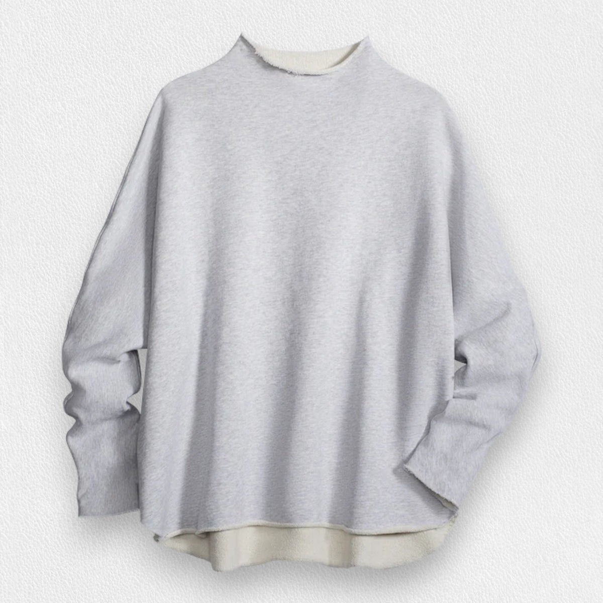 A woman with long brown hair stands smiling near a black grand piano in a modern, well-lit room. She wears the FRANK AND EILEEN - EFFIE LONG SLEEVE FUNNEL NECK CAPELET from FRANK &amp; EILEEN paired with blue jeans. A large window and a lamp are in the background, enhancing the cozy winter warmth of her stylish ensemble.