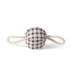 The FRINGE STUDIO - PAINTED GINGHAM PULLING DOG TOY from PET SHOP BY FRINGE STUDIO features a spherical black and white plaid fabric center made of cotton canvas, with two white twisted rope handles extending from opposite sides. Non-toxic inks ensure safety while the TPR spikey squeakerball inside adds an element of fun. The toy is set against a plain white background.