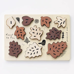 The WEE GALLERY - COUNT TO 10 WOODEN TRAY PUZZLE WITH LEAVES by WEE GALLERY is a wooden puzzle that includes ten oak leaf-shaped pieces in various shades of brown. Each piece fits into a light-colored wooden board adorned with minimalist drawings of trees and a bird. This educational toy is designed to enhance counting skills, featuring the text "Count to Ten" on the board.