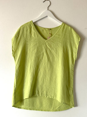 The CUT LOOSE - V NECK BOXY TOP in sage green, made from breezy linen, hangs on a white hanger against a plain light-colored wall. A tag is attached to the neckline of this short-sleeved garment, making it perfect for your summer wardrobe.