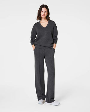 A person wearing SPANX - AirEssentials Brushed Straight Leg Pants in dark gray is facing away from the camera. Their hands are casually placed in the pockets, and they're paired with light-colored shoes. Designed from breathable 4-way stretch fabric, these pants provide ultimate comfort against a plain white background.