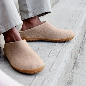 The GLERUPS - SLIP ON SHOE WITH RUBBER SOLE IN SAND by GLERUPS, a beige wool slipper with a closed toe and natural rubber sole, is shown slightly elevated against a white background with a faint shadow beneath.