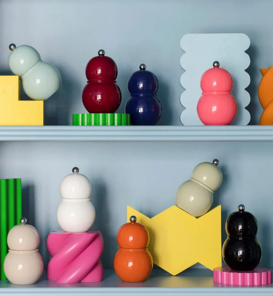 ADDISON ROSS LONDON's CHUBBIE salt or pepper mills, shaped like colorful gourds, rest on shelves with playful geometric designs. With a ceramic mechanism, these vibrant 12cm pieces stand out against a muted blue background.