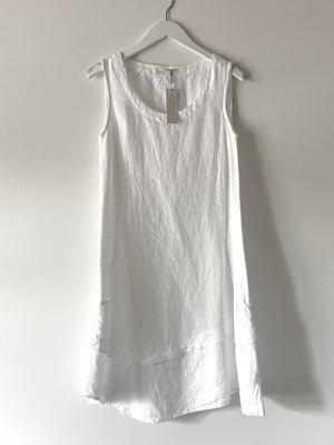 The CUT LOOSE - TUNIC DRESS by CUT LOOSE, a sleeveless white linen garment, hangs on a white hanger against a light gray background. This lightweight summer piece features a round neckline and has a label attached to the neckline area, indicating it is new.