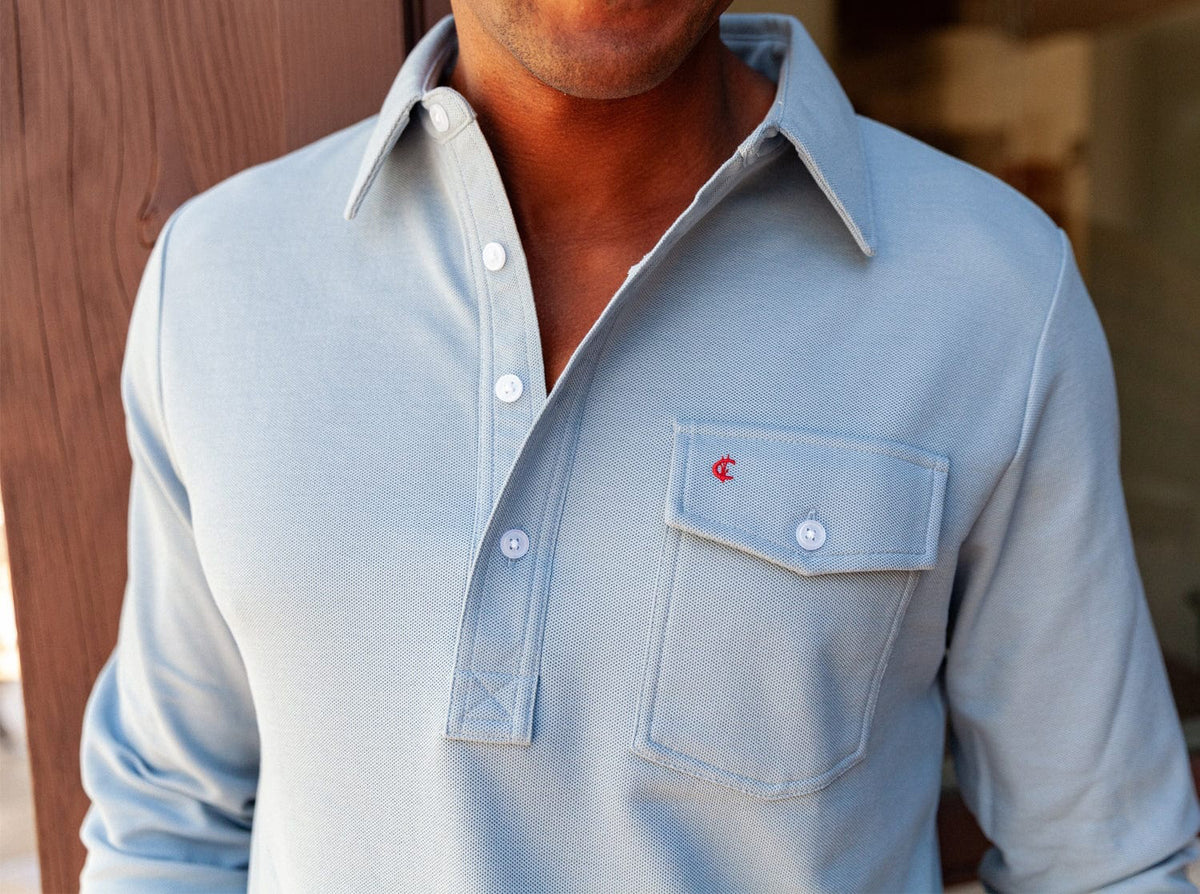 A smiling man with short blond hair and a beard wears the CRIQUET Long Sleeve Players Polo Shirt in Mr Freeze, standing against a plain white background.