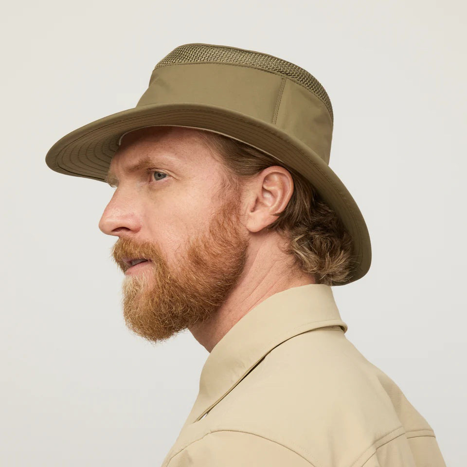 A man with a red beard and wavy hair, wearing a tan button-up shirt and a TILLEY AIRFLO Medium Brim LTM5 hat by TILLEY, is shown in profile against a plain light background.