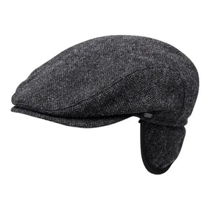 The WIGENS IVY SLIMP HERRINGBONE CAP is a dark gray Shetland wool flat cap with ear flaps, shown in side view on a white background.