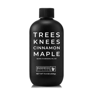 A black bottle with a matching black cap labeled "BUSHWICK KITCHEN - 'TREES KNEES' CINNAMON MAPLE SYRUP" in white text. This 11.5 oz (326g) delight from Bushwick Kitchen combines the rich flavors of cassia cinnamon and pure maple syrup. The label proudly announces that this product was born in Brooklyn, NY.