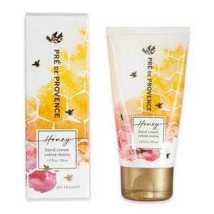 Image of a honey-scented "Honey Hand Cream" tube and its packaging box by European Soaps, LLC. The white tube and box showcase a honeycomb pattern, bees, and pastel floral designs in yellow, orange, and pink hues. Text on the packaging reads "Pré de Provence Honey Hand Cream," indicating a product of France made with Organic Honey.