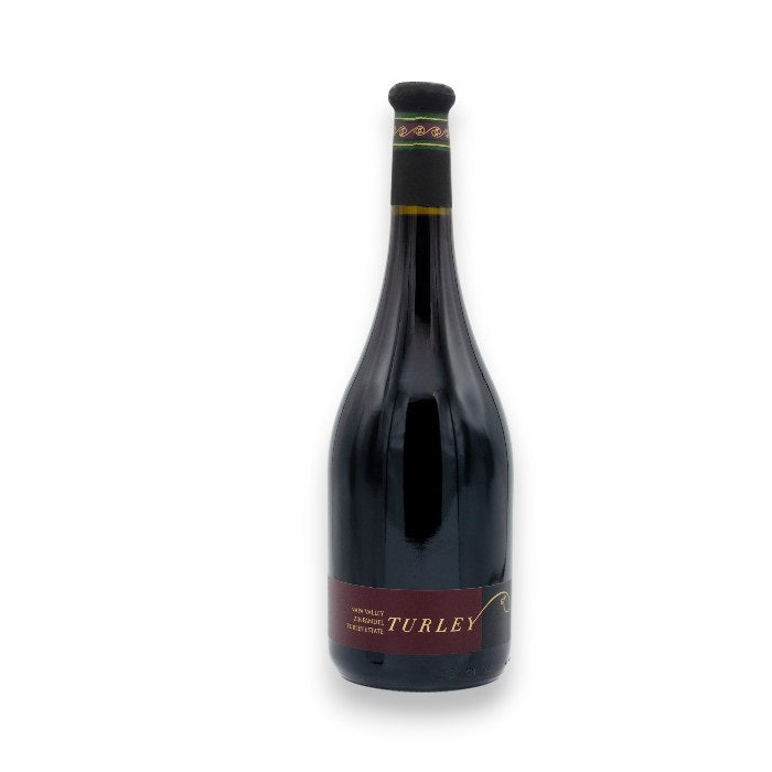 A bottle of Turley Estate Zinfandel 2022, a fine field blend from Napa Valley, sports a dark glass body with a red and yellow label. The tall neck has a dark cap with a decorative band near the top. 