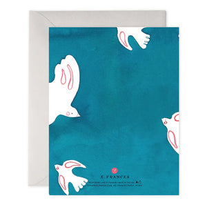 The PEACE DOVES HOLIDAY CARD by E.FRANCES PAPER features a handcrafted watercolor design of lovely white doves holding olive branches on a teal background, with "Peace on Earth" elegantly scripted in gold. This exquisite card is partially nestled inside a light gray envelope and proudly made in the USA.