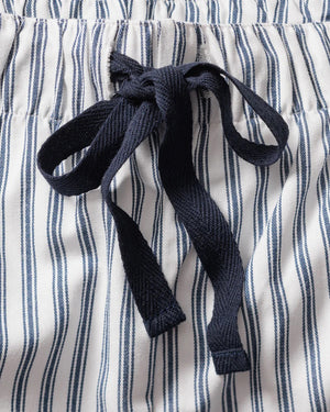 The FEARRINGTON LIFESTYLE COLLECTION - MENS TWILL NAVY FRENCH TICKING PAJAMAS by PETITE PLUME is neatly folded and displayed. This striped pajama set, made from the finest quality cotton, features white and navy blue vertical stripes in a traditional French ticking design with a small embroidered sheep on the chest pocket. It has a collar, buttons, and an attached hang tag with branding.