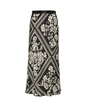 The MIRTO 1956 - BLACK AND WHITE PRINT MIDI SKIRT by MIRTO 1956 features a black A-line silhouette with an intricate white floral squares patchwork design set within diamond shapes. This skirt has a slight flare, providing a flowy appearance, and its symmetrical pattern offers a balanced and flattering chic look.